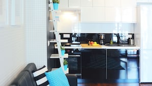 Cocina moderna con armarios blancos, encimera negra y lavavajillas empotrado. Hay un estante de madera con plantas en macetas y una escalera para almacenamiento.