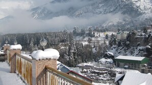 A snowy mountain landscape with a town in the valley below. - Sarthak Regency (Manali)