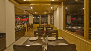 A restaurant with wooden interior, tables set for dining, and a view through the window. - Sarthak Regency (Manali)