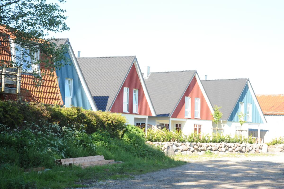 A row of colorful houses with sloped roofs, a stone wall, and a gravel path.