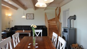 Een eetruimte met een houten tafel, witte stoelen, een vaas met bloemen en een trap naar een hoger niveau.