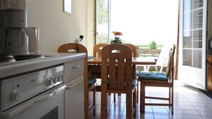 Een keuken met een fornuis, kasten en een eethoek met stoelen en een tafel.
