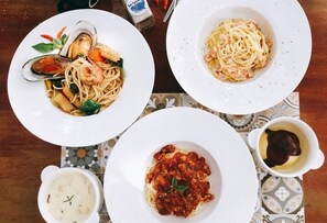 A table with three plates of pasta dishes, a bowl of soup, and a small dish of sauce. - Nithiporn Resort (Ranong)