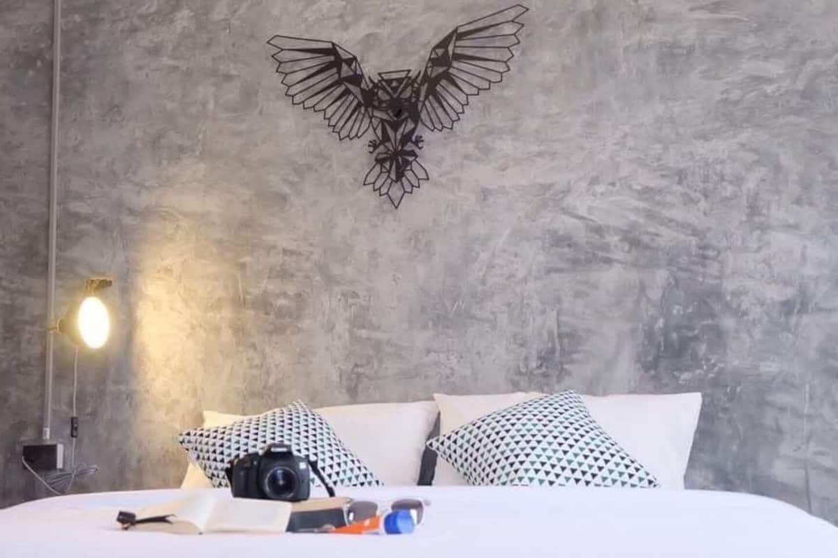 A bedroom with a bed, pillows, a camera, and a wall-mounted light fixture.