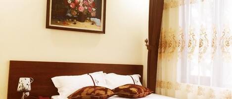Una habitación de hotel con una cama, una mesita de noche, una lámpara, un cuadro y una ventana con cortinas.