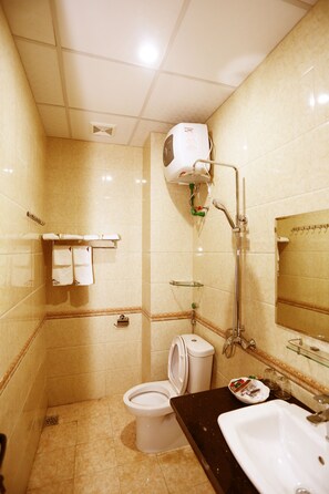 Ein Badezimmer mit Toilette, Waschbecken und Dusche. An der Wand befinden sich ein Handtuchhalter und ein Spiegel.