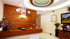 A hotel reception desk with a wooden finish, a clock, and a sign indicating 'Reception'. - Tiamo Hotel Ha Giang (Ha Giang 2)