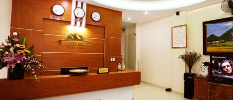 A hotel reception desk with a wooden finish, a clock, and a sign indicating 'Reception'.