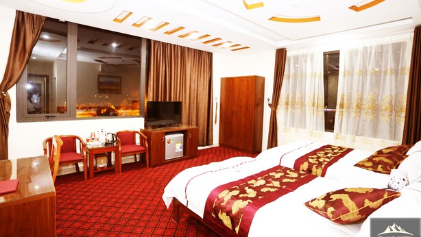 A hotel room with a large bed, a desk with a chair, a television, and a wardrobe. - Tiamo Hotel Ha Giang (Ha Giang 2)