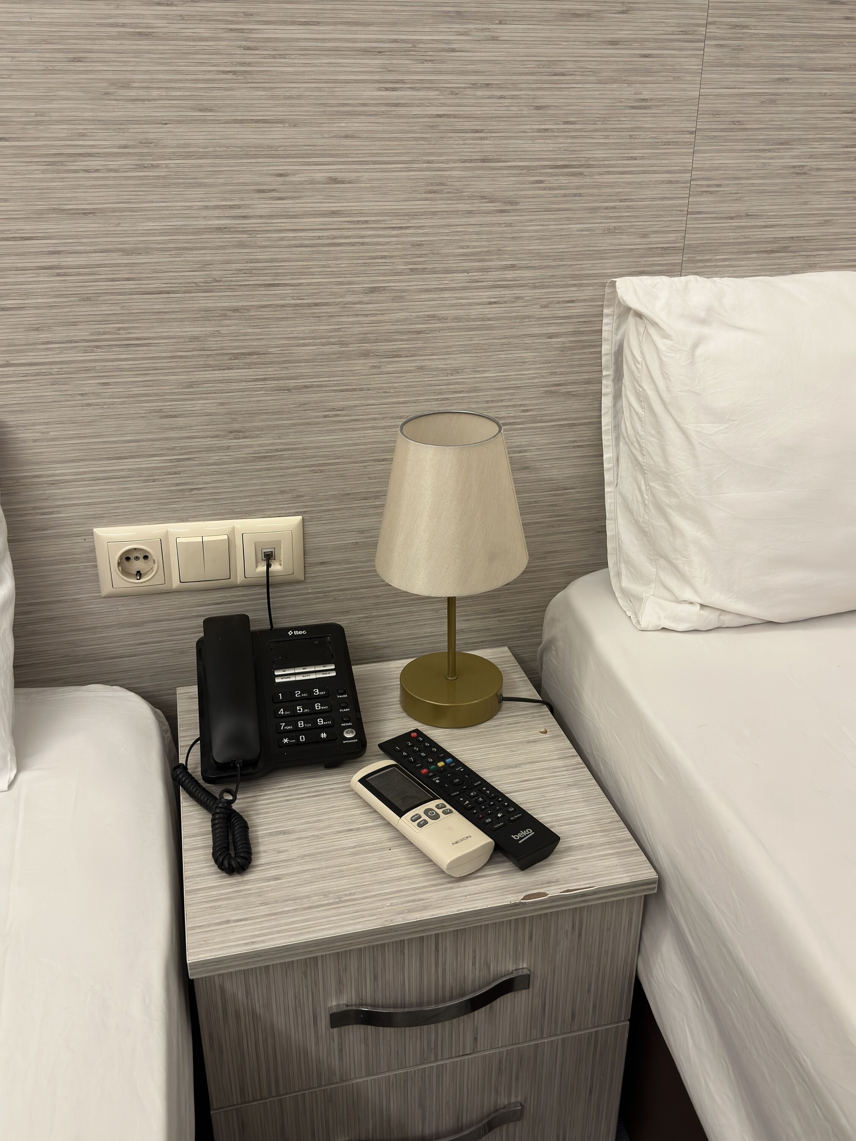 Una habitación de hotel impecable con una cama, una mesita de noche con lámpara, teléfono y control remoto.