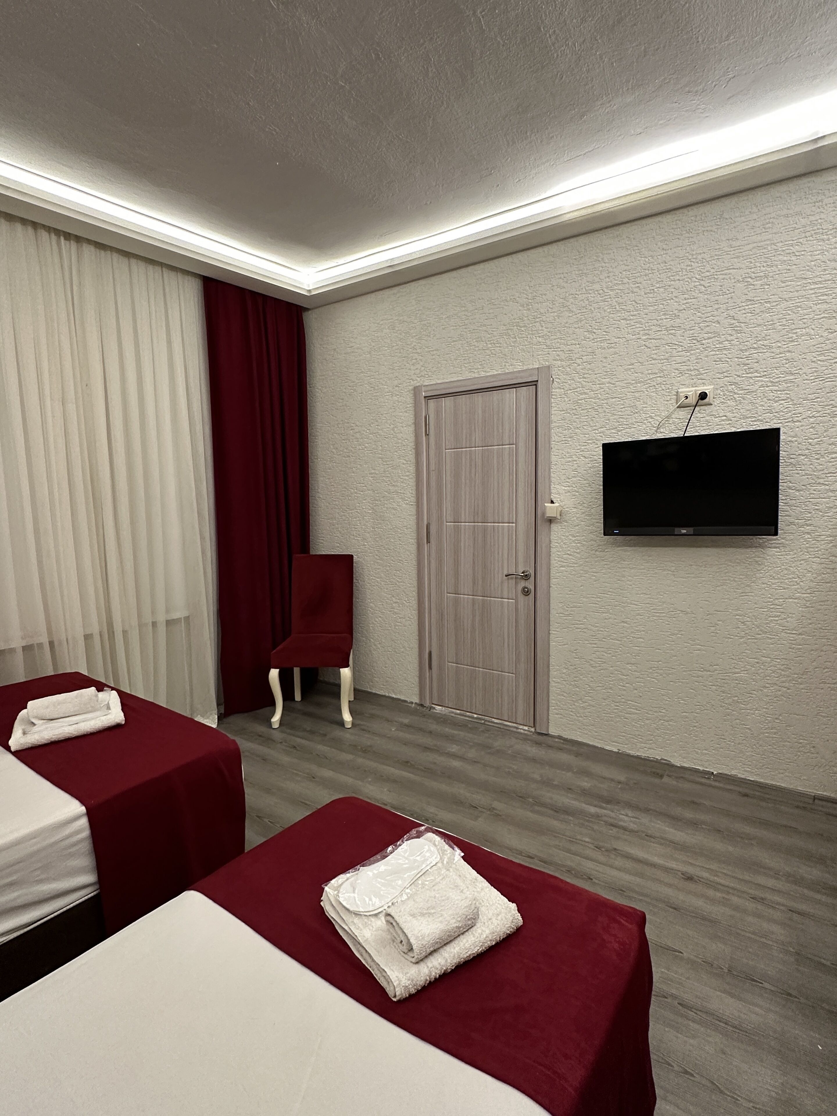 Habitación de hotel con dos camas, un televisor montado en la pared, una puerta y una ventana con cortinas.