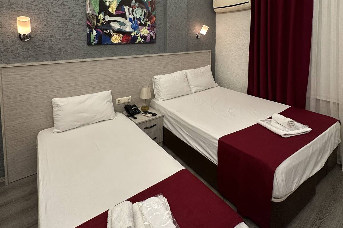 A hotel room with two beds, a painting on the wall, and a red curtain.