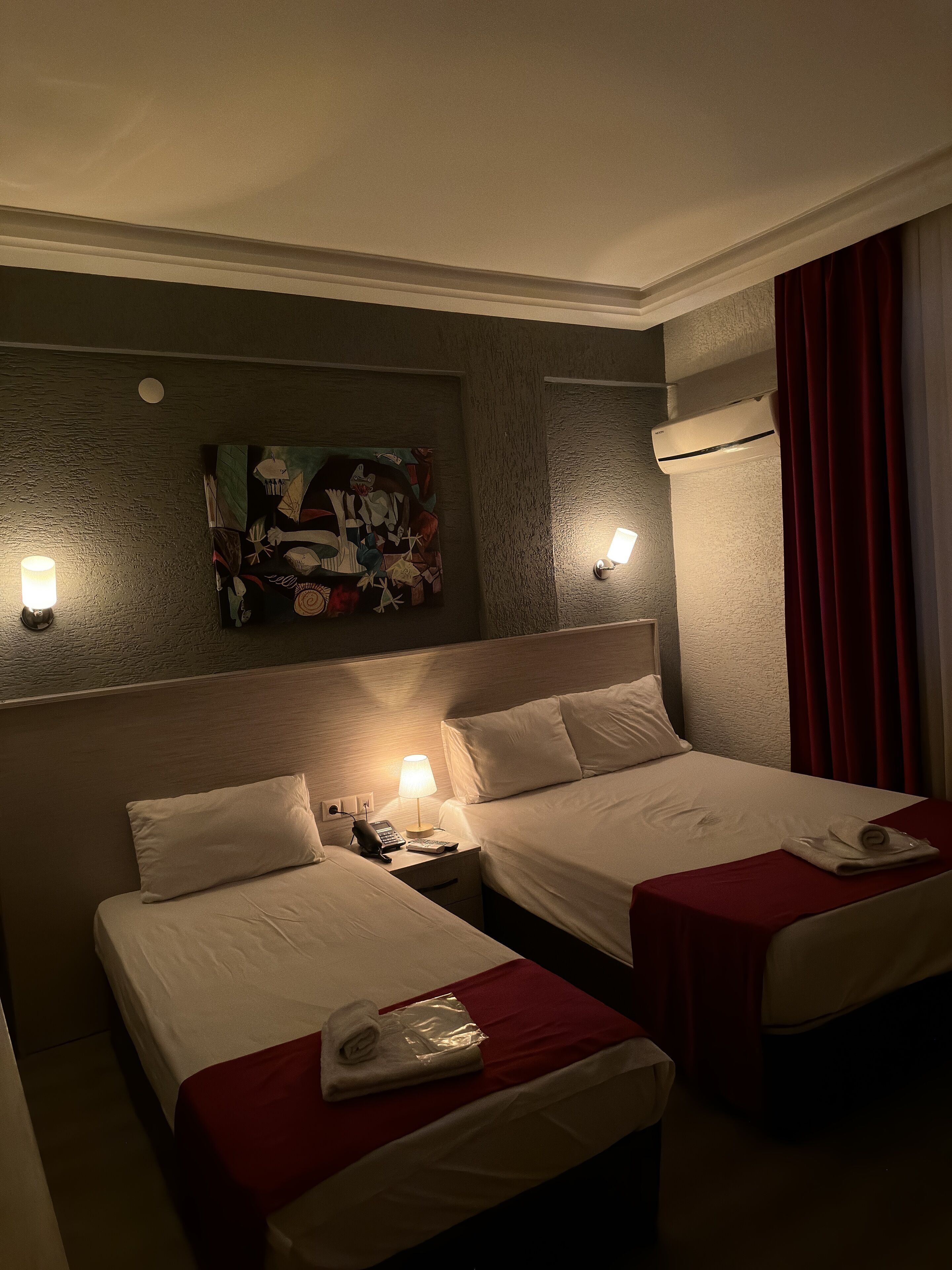 A hotel room with two beds, a painting on the wall, a lamp, and a telephone on the nightstand.