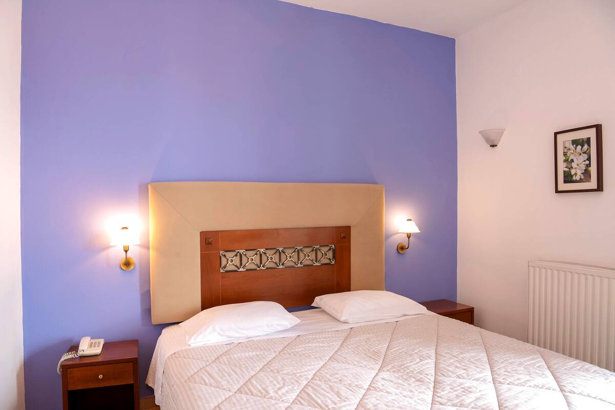 Una habitación de hotel con una cama individual, una mesita de noche con teléfono y dos lámparas fijadas a la pared.
