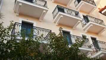 Un edificio de varios pisos con balcones, cada uno con barandilla de hierro forjado negro y una ventana con persiana azul.