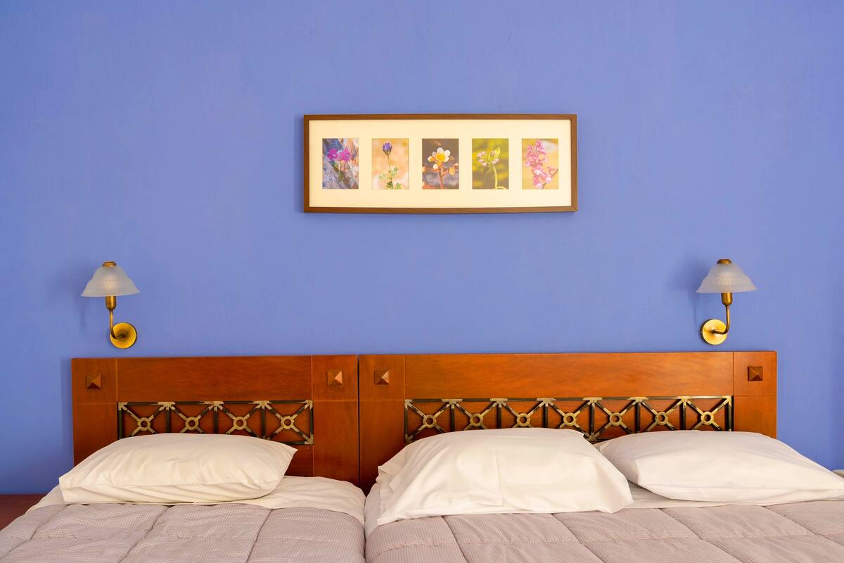 Cama doble con cabecera de madera, dos lámparas de noche y una obra de arte floral enmarcada en la pared.