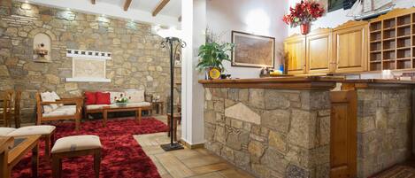 A cozy interior with a stone wall, wooden furniture, a red rug, and a kitchen area with wooden cabinets.