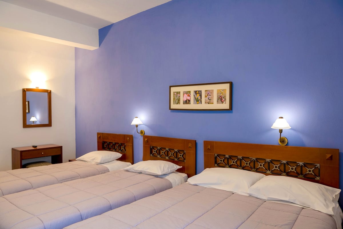 Una habitación de hotel con dos camas, una mesita de noche, una lámpara y un cuadro en la pared.