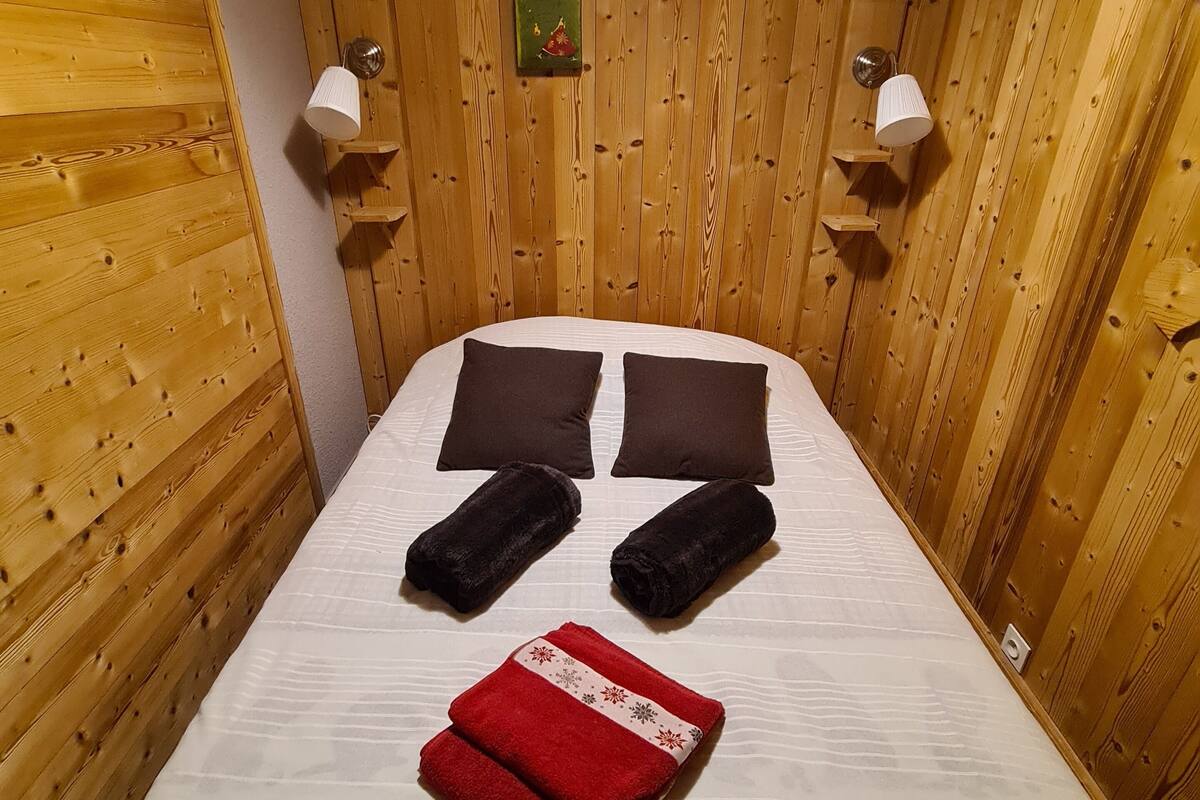 A wooden-paneled room with a bed, two wall-mounted lamps, and a small decorative item on the wall.