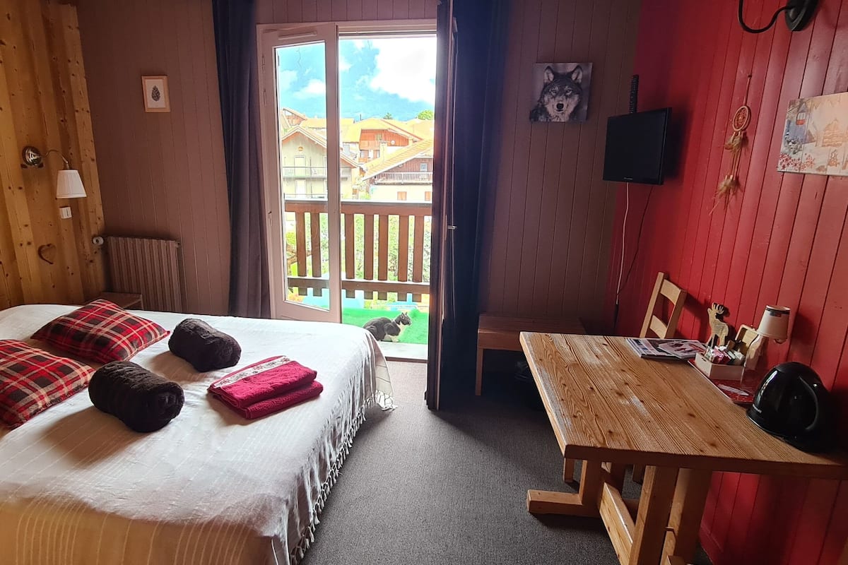 A cozy room with a bed, a wooden table, and a red wall.