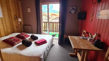 A cozy room with a bed, a wooden table, and a red wall.