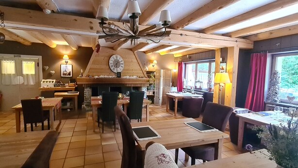A cozy dining area with wooden tables and chairs, a central fireplace, and a clock on the wall. - Hôtel Restaurant L'Adray (Aime-la-Plagne)