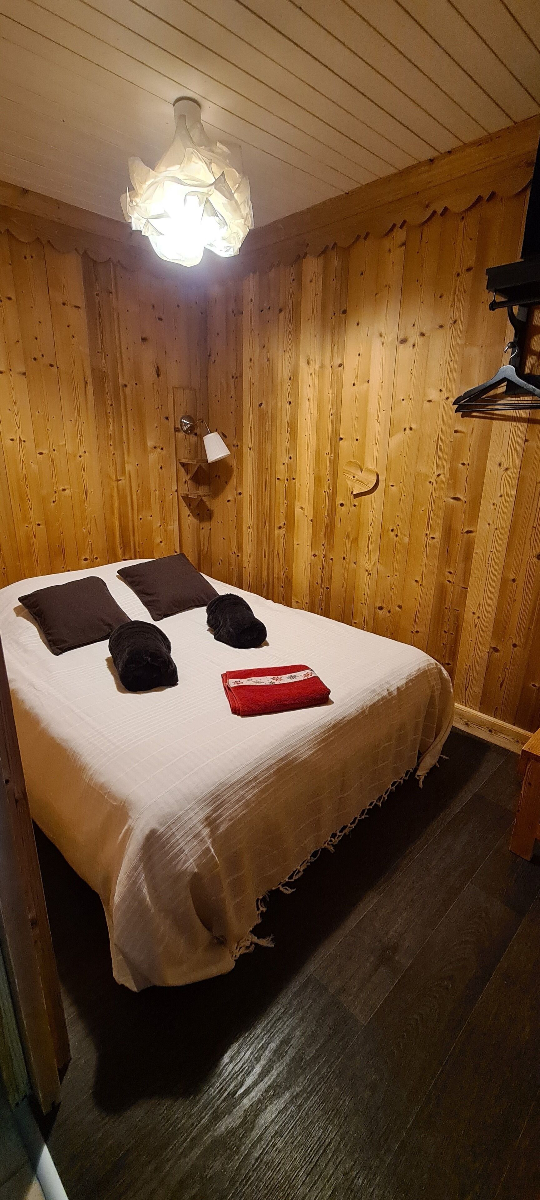 A wooden-paneled room with a bed, a hanging light fixture, and a wall-mounted shelf.