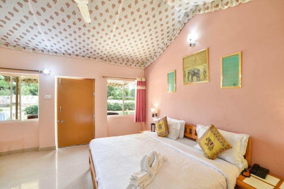 A hotel room with a bed, a bedside table with a lamp, a window with curtains, and framed pictures on the wall.