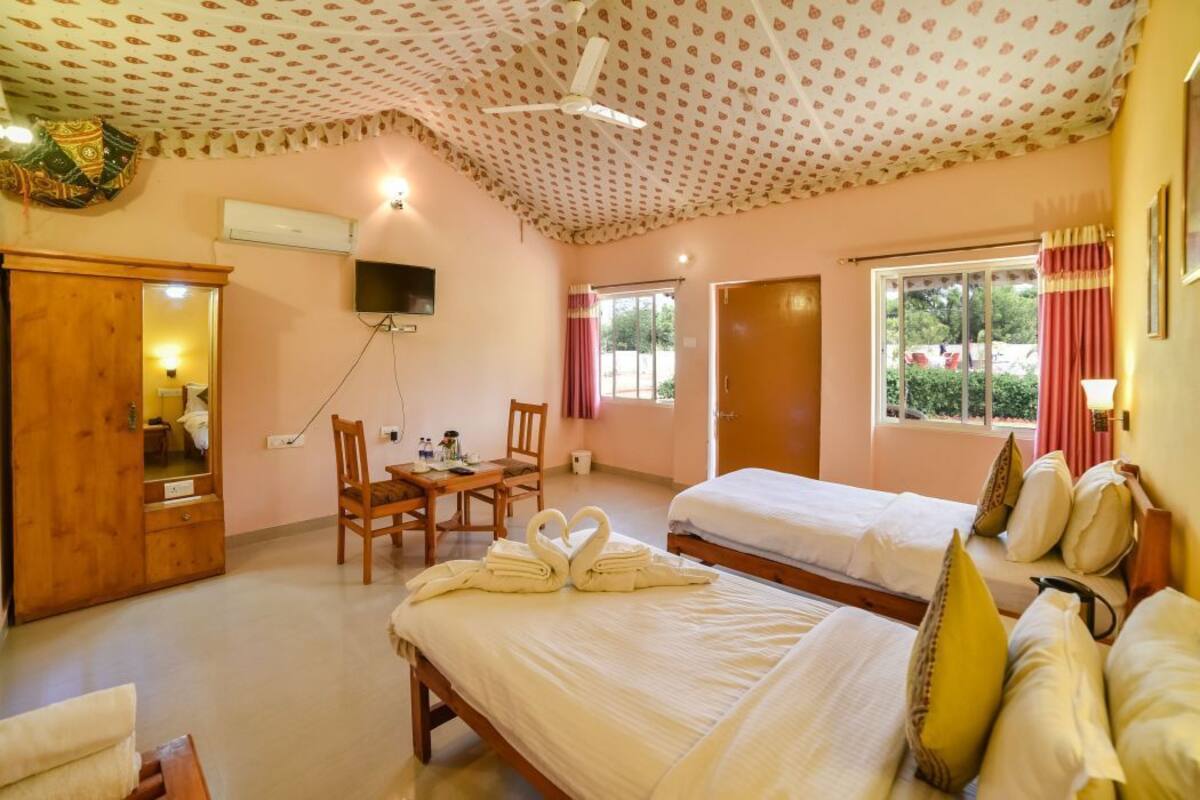 A hotel room with two beds, a desk with chairs, a television, and a ceiling fan.