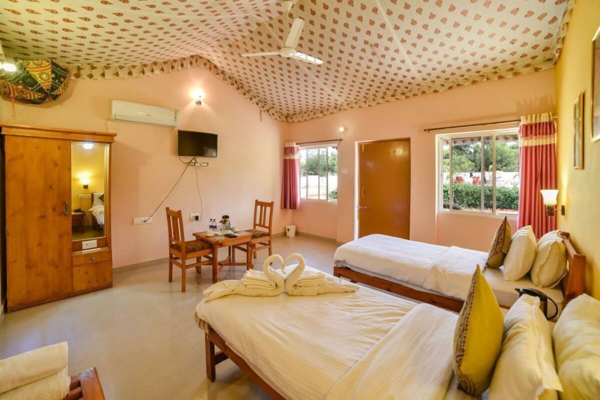 A hotel room with two beds, a desk, a chair, a TV, and a ceiling fan.