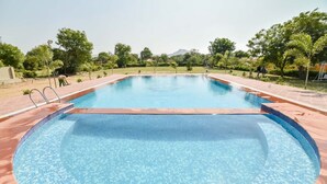 A rectangular outdoor swimming pool with a tiled edge, surrounded by a brick patio and greenery. - Pushkar Rajwara Resort (Pushkar)