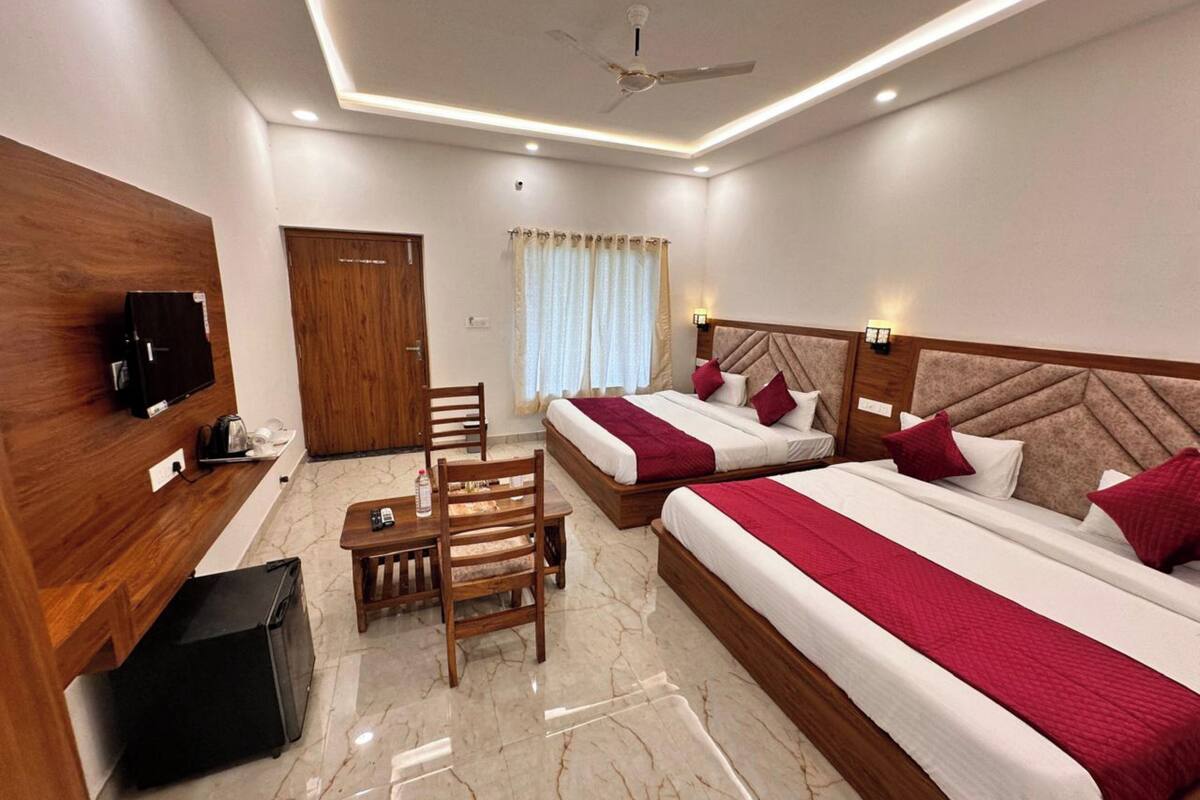A hotel room with two beds, a desk, a chair, a TV, and a ceiling fan.