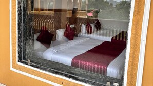A framed window with a view of a traditional building and a bed with white and red bedding. - Pushkar Rajwara Resort (Pushkar)