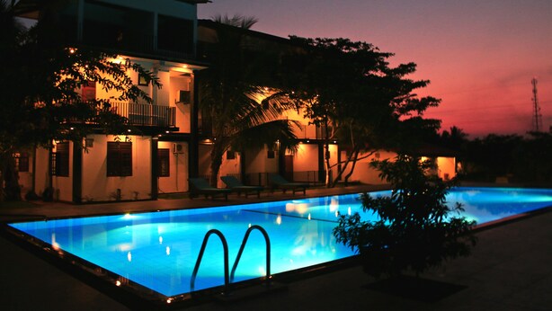 A swimming pool with a modern building in the background. - Hotel Freedom Village (Dambulla)
