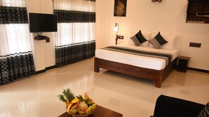 A hotel room with a bed, a TV, a bedside table with a fruit bowl, and a sofa. - Hotel Freedom Village (Dambulla)