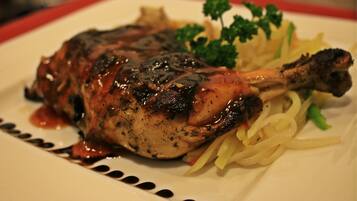 A roasted chicken leg with sauce, garnished with parsley, served on a plate with pasta.