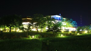A building with multiple illuminated sections, surrounded by trees and a grassy area. - Hotel Freedom Village (Dambulla)