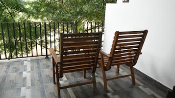 A wooden bench and table on a balcony with patterned flooring and a view of trees.
