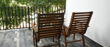Un banco de madera y una mesa en un balcón con suelo estampado y vista a árboles.