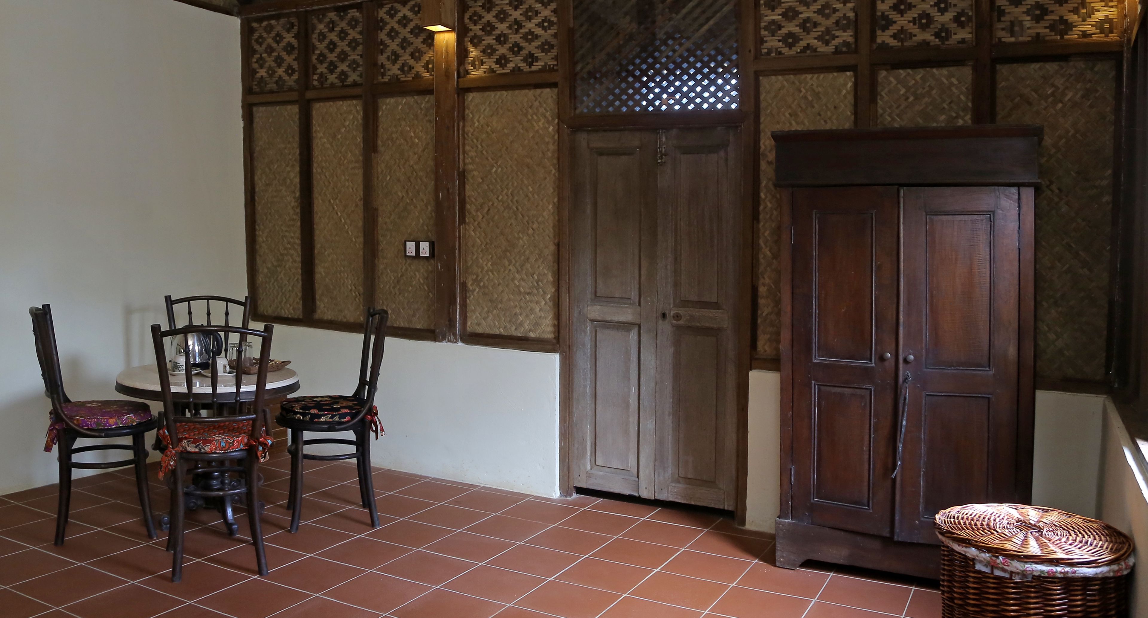Une pièce avec un sol carrelé, une table ronde entourée de chaises, un meuble en bois et un panier en osier.