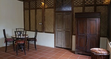 Una habitación con piso de baldosas, una mesa redonda con sillas, un armario de madera y una cesta tejida.