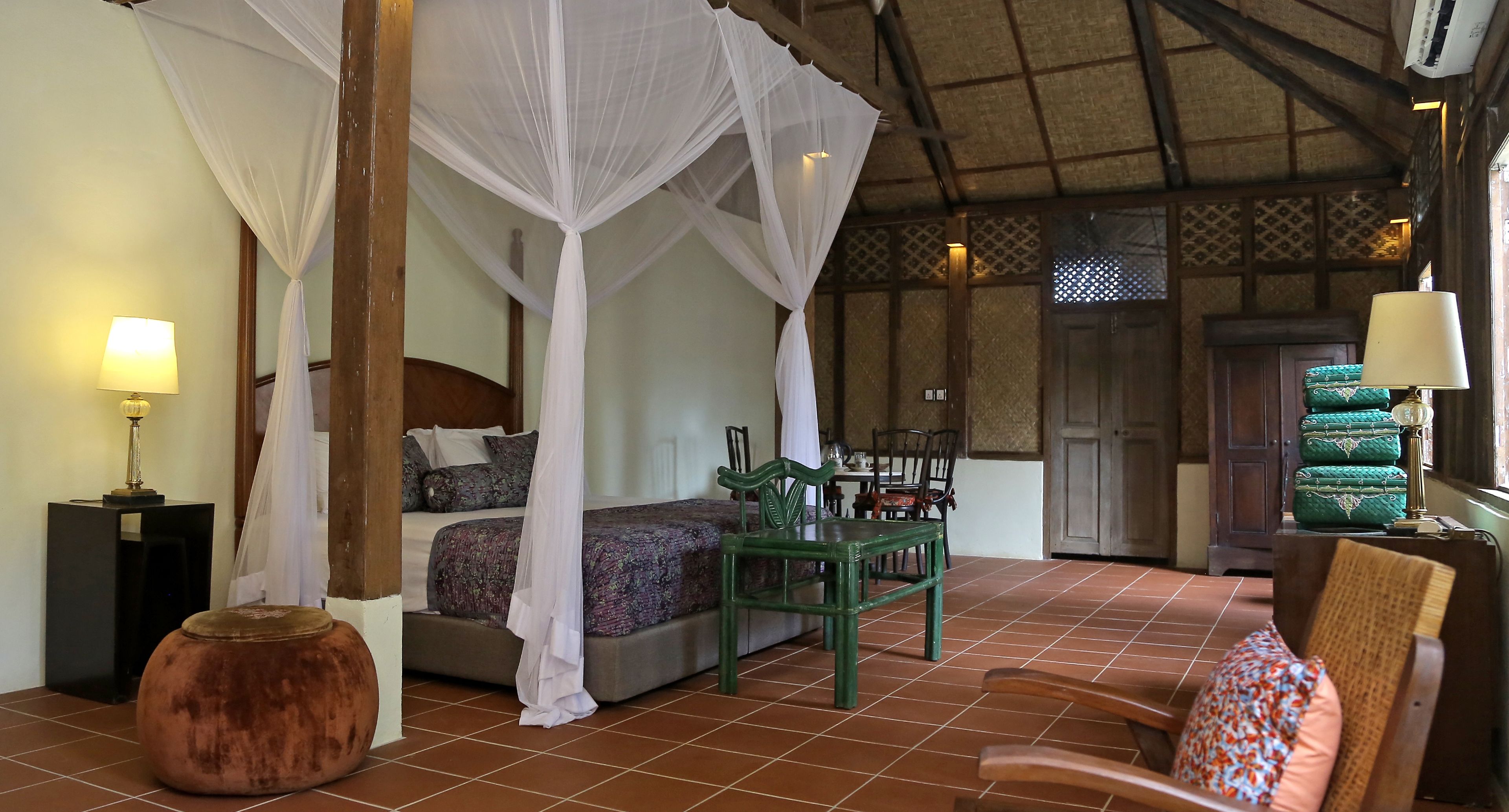 A room with a bed under a canopy, a dining table with chairs, a large vase, and a lamp.