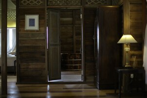 Un interior de madera con una puerta que da a una habitación, un cuadro en la pared y una mesa con una lámpara.