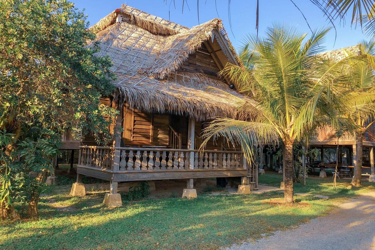 A wooden house with a thatched roof and a wooden balcony.