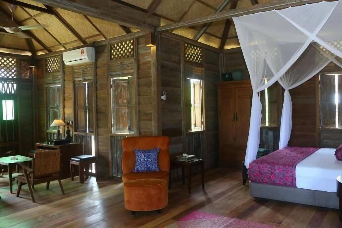 A wooden cabin-style room with a bed, a chair, a table, and a window.