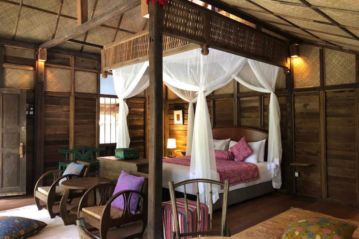 A four-poster canopy bed with white drapes, wooden walls, and a small table with chairs.