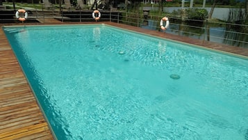Una piscina rectangular con agua cristalina, rodeada por una terraza de madera. Se observan chalecos salvavidas en el borde de la piscina.