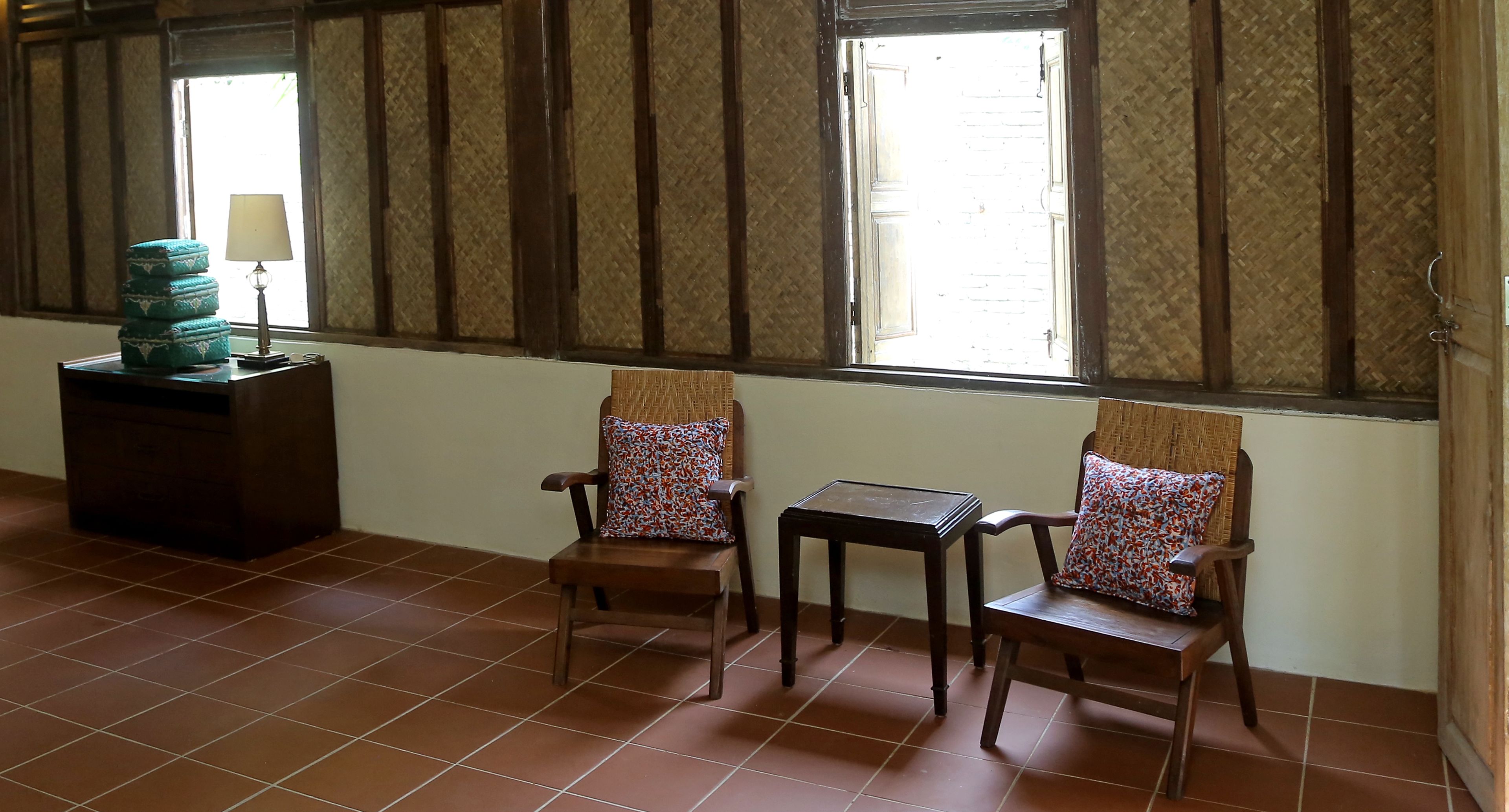 A room with two wooden chairs, a small table, and a stack of blue boxes on a wooden cabinet.