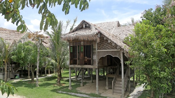 A traditional wooden structure with a thatched roof, surrounded by palm trees and greenery. - Kunang-Kunang Heritage Villas (Langkawi)
