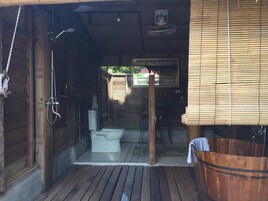 A wooden cabin with a bathroom featuring a toilet, shower, and a wooden bathtub.